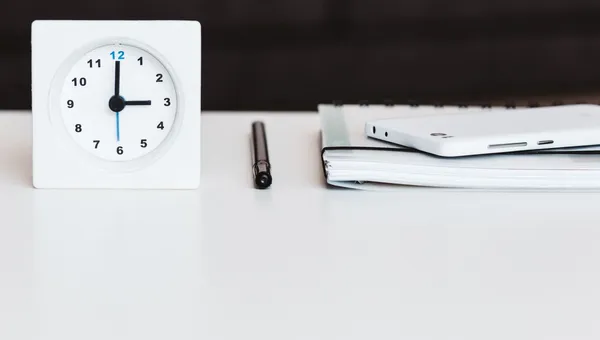 Reloj de escritorio blanco junto a una libreta y un bolígrafo