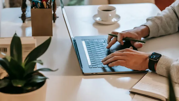 Persona trabajando desde casa en una laptop junto a una taza de café y una libreta