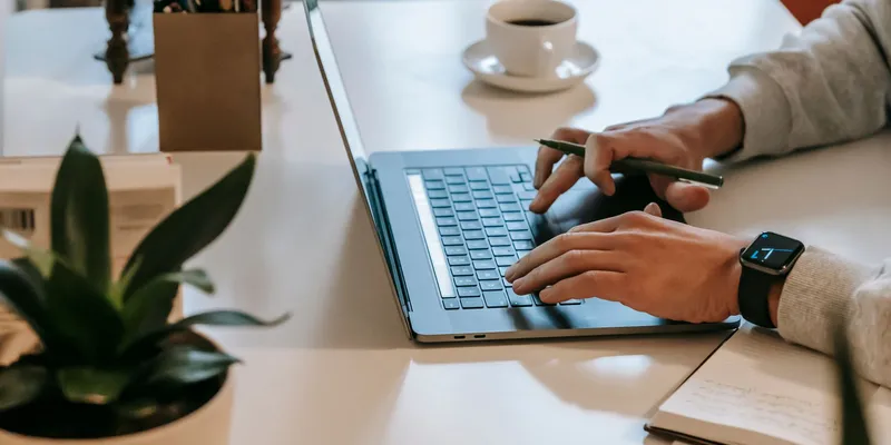 Persona trabajando desde casa en una laptop junto a una taza de café y una libreta