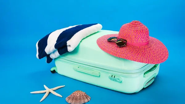 Maleta abierta con sombrero, toalla y artículos de playa listos para vacacionar
