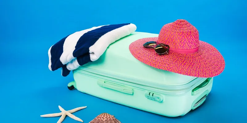 Maleta abierta con sombrero, toalla y artículos de playa listos para vacacionar